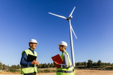 Rüzgar türbinleri olan bir alanda yenilenebilir enerji mühendisleri iş gününü planlıyorlar. Yenilenebilir enerji kavramı.