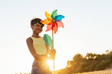 Güzel kız yaz güneşinin altında elinde renkli bir fırıldak tutarken mutlulukla ışıldıyor..