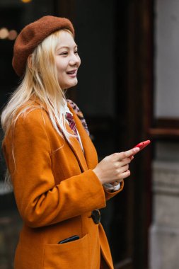 Cep telefonunu açık havada tutarken gülümseyen şık bir kadın. Teknoloji konsepti.