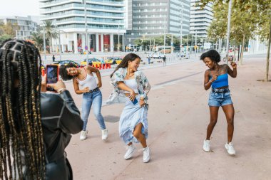 Çok ırklı ve cinsiyetli arkadaşlar sokakta dans ederken video kaydediyorlar.