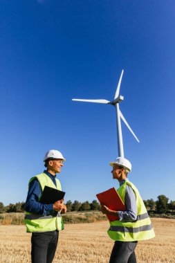 Erkek ve kadın mühendisler kırsal bir rüzgar çiftliğinde çalışarak elektrik üretmek ve çevreyi korumak için yenilenebilir enerji kullanıyorlar..