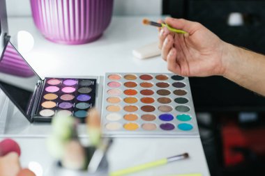 Renkli bir göz farı paletiyle makyaj yapan bir adamın yakın plan görüntüsü..