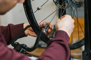 Bir dağ bisikletinin arka tekerleğindeki tellerin gerilimini ayarlamak için bir alet kullanarak mekanik ellerin yakın çekim görüntüsü..