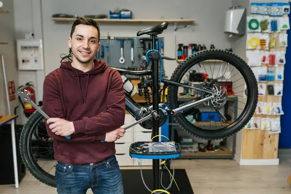 A photo of a bike mechanic in his bicycle workshop, picking up tools with a bicycle behind him and the workshop in the background