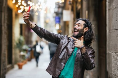 Neşeli adam dışarıda cep telefonuyla selfie çekerken gülümsüyor. Teknoloji konsepti.