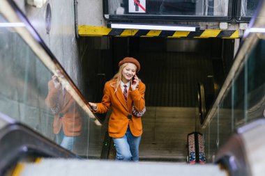 Metro istasyonundan ayrılırken Asyalı bir kadın telefonda konuşuyor. Teknoloji ve ulaşım kavramı.