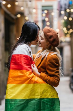 Sokakta Igbt gökkuşağı bayrağına sarılmış lezbiyen çift öpüşüyor. LGBT kavramı.