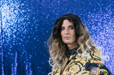 Kendinden emin bir travesti, ışıltılı bir arka planda poz verirken kameraya bakıyor. LGBT kavramı.