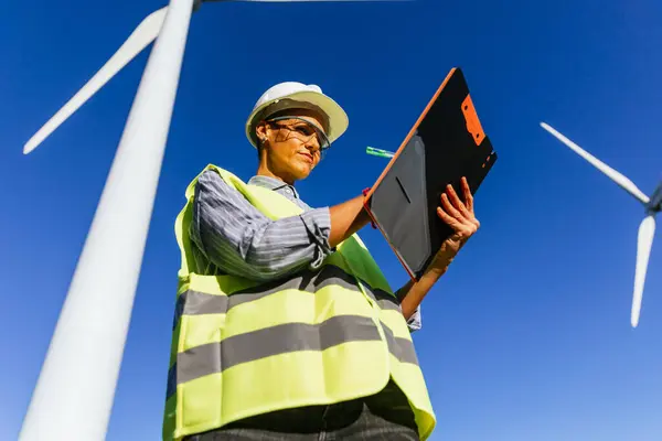 An engineer on a windmill for the production of clean renewable energy, she looks focused as she fills out a report.