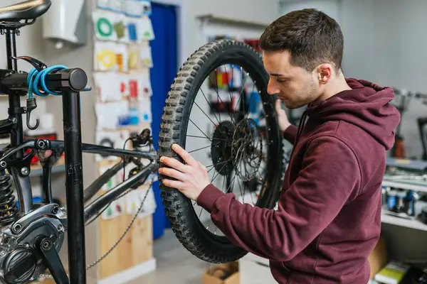 Bike mechanic changing and examining a rear wheel of a mountain bike in his workshop.