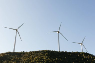 Rüzgarda zarifçe dönen üç rüzgar türbini bir tepenin üzerinde dimdik duruyor. Doğal manzara, gökyüzü ve ışık bu rüzgar çiftliğinin güzelliğini arttırır, hafif esintiden elektrik üretir.