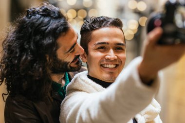 Birbirlerinin önünde duran iki adam, her biri fotoğraf çekmek için bir kamera ya da akıllı telefon tutuyorlar. Kamera ayarlarını ayarlamaya ve çekim için poz vermeye odaklanmışlar..