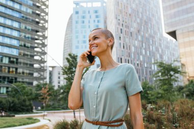 Bir iş kadını, yüksek binalar ve hareketli şehir hayatı ile çevrili işlek bir caddede yürürken bir telefon görüşmesi yapar..