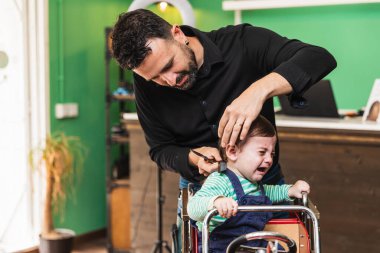 Profesyonel kuaför enerjik bir berber dükkanında sıkıntılı bir çocuğun saçını nazikçe kesiyor.