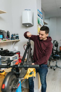 Bisiklet atölyesinde elektrikli scooter hazırlayan bir tamircinin dikey fotoğrafı..