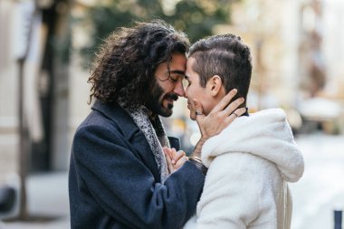 Homoseksüel bir çift arasında, sevgi dolu bir kucaklama ve şehir arka planında sevgi dolu bir bakış gösteren şefkatli bir an.
