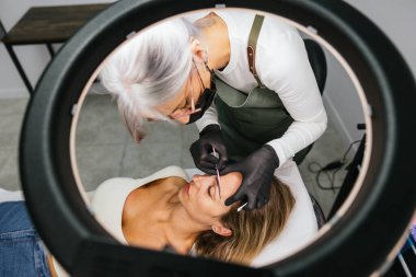 Güzellik uzmanı profesyonel mikropatinaj tedavisine başlamadan önce bir müşterinin kaş tasarımını titizlikle özetliyor.