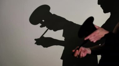 Detaylı el hareketleri ve boş bir duvardaki aksesuarlarla gizemli bir hikaye anlatıcısının gölge kuklaları performansı.