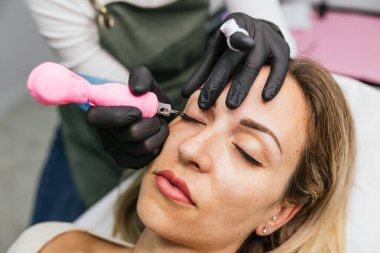 Profesyonel göz kalemi mikro pigmentasyon prosedürü. Bir kozmetik kliniğinde, kalıcı makyaj hassasiyeti kullanan bir kadın güzellik uzmanı tarafından.