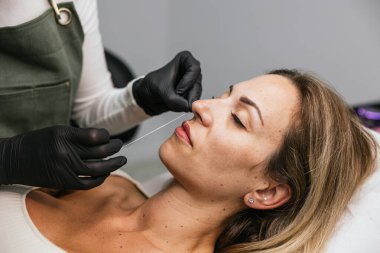 Estetisyen, güzellik kliniğindeki gevşemiş bir bayan müşterinin üzerinde hassas bir ip iziyle dudak pigmentasyonu yapıyor.