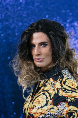 Göz kamaştırıcı bir travestinin portresi ışıl ışıl mavi bir arka plana karşı, cesur makyaj ve moda