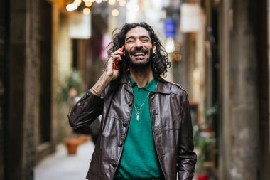 Genç yaratıcı profesyonel sokakta yürüyor, cep telefonuyla konuşurken gülüyor.