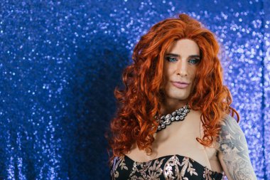 Confident drag queen with vibrant red hair against a sparkling blue background clipart