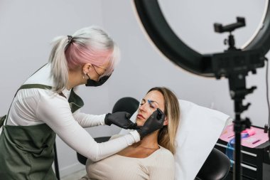 Güzellik uzmanı modern bir kuaförde mikro patinaj tekniği kullanarak müşteriye kaş dövmesi yapıyor.
