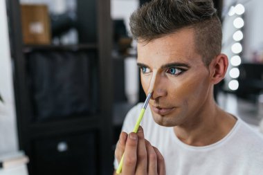 Aynalı bir soyunma odasında makyaj uygulamasına odaklanan sanatçı