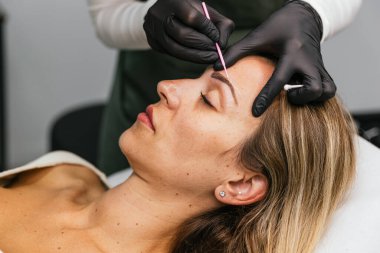 Profesyonel güzellik uzmanı, müşterilerine mikroptan önce makyajlı kaşlar hazırlıyor, gelişmiş bir yüz özelliği için hassas tasarım ve simetri sağlıyor.