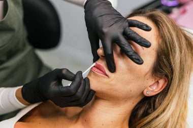 Profesyonel güzellik uzmanı, kadın bir müşteriye mikro pigmentasyon tedavisi yapılmadan önce dudak tasarımı için iplik işaretlemesi yapıyor.