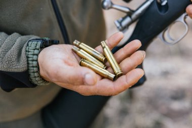 Avcı elinde tüfek fişekleri tutuyor, tüfeği de arka planda görünüyor.