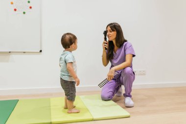 Göz doktoru, göz hekimliği kliniğinde tıbbi bir randevu sırasında bir çocuğun görme yetisini incelemek için retinoskop kullanıyor.