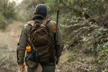 Hunter, bir tüfek ve sırt çantasıyla dolu sık bir orman yolunda ilerliyor.