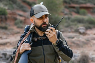 Hunter ormanda omzunda tüfek taşırken telsiz kullanıyor.