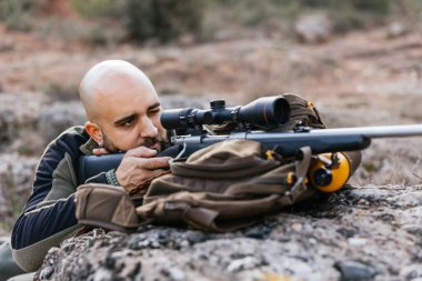 Avcı, doğal bir ortamda av sırasında dürbünlü tüfeğiyle yere yatar.