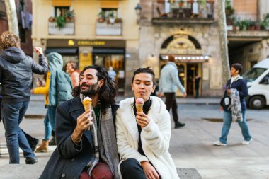 Barselona şehir merkezindeki bir bankta oturmuş dondurma yiyen mutlu eşcinsel çift yaşam tarzlarının tadını çıkarıyorlar.