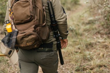 Avcı ormanı bir tüfek ve sırt çantasıyla geziyor, sonbahar ortamına karışıyor.