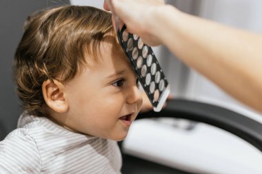 Göz doktoru, göz muayenesi sırasında gülümseyen bir çocuğun alnına retinoskop tutuyor.