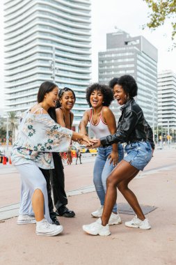 Dört neşeli kadın ellerini birleştiriyor, gülüyorlar ve şehirde birlikte vakit geçiriyorlar.