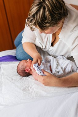 Sevgi dolu bir anne yeni doğmuş bebeğiyle üstünü değiştiriyor beyaz bir paspasın üzerinde yatıyor.