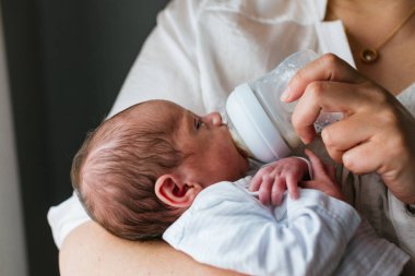 Annesi sevgi dolu bir şekilde bir aylık bebeğini süt şişesiyle besliyor ve bir bağ ve bakım anı yaratıyor.