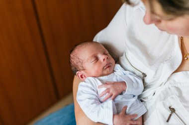 Yeni doğmuş bebek, annesinin kollarında huzur içinde uyuyor. Aile sıcaklığında sevgi ve bağlılık dolu bir anı kutluyor.