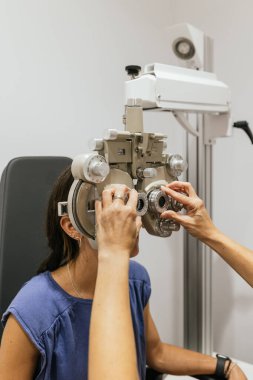 Göz doktoru, bir muayenehanede göz muayenesi sırasında bir hastanın yüzündeki phoropter 'ı ayarlıyor.