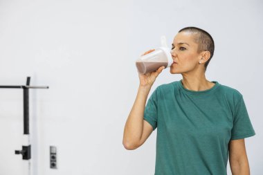 Yetişkin bir kadın spor salonundaki yoğun bir eğitimden sonra protein içeceği içiyor. Aktif yaşam tarzı için iyileşme ve su ihtiyacını karşılıyor.