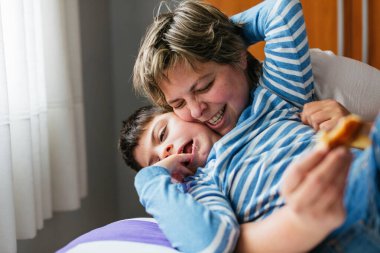 Happy mother playing and tickling her son with cerebral paralisis on a bed, embracing him with love and joy, creating tender moments of togetherness clipart