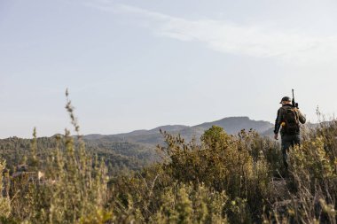 Avcı tüfeğini taşıyor ve kamuflaj takıyor. Vahşi doğada yürüyor.
