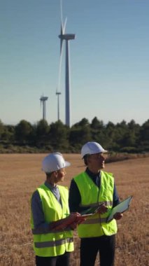 Rüzgar türbinlerinin önünde veri tartışan mühendisler, sürdürülebilir enerji çözümleri için birlikte çalışıyorlar