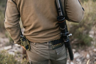 Avcı bir tüfekle ormanda yürüyor, doğada maceraya hazır.