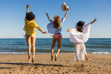 Üç etnik çeşitlilikte kadın güneşli bir sahilde neşeyle atlıyor, yaz tatillerini kutluyor ve birlikte kaygısız anları kucaklıyor.